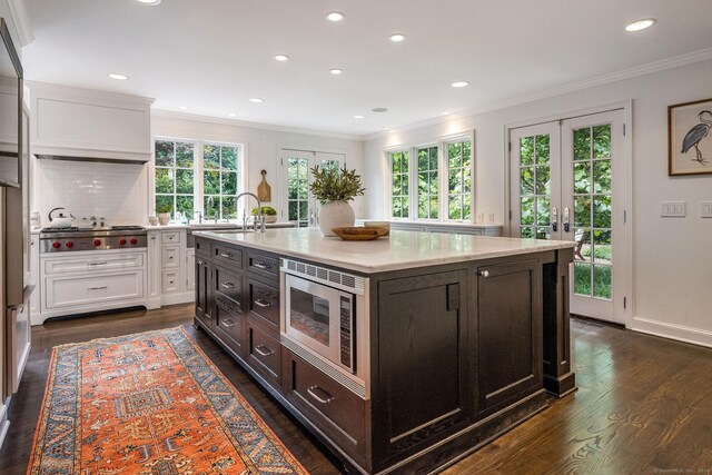 kitchen with an island with sink, dark hardwood / wood-style flooring, stainless steel appliances, and white cabinets