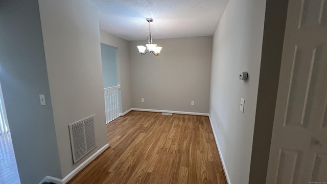 unfurnished dining area featuring a notable chandelier, wood-type flooring, and a textured ceiling