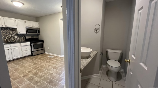 interior space featuring decorative backsplash, white cabinets, and appliances with stainless steel finishes