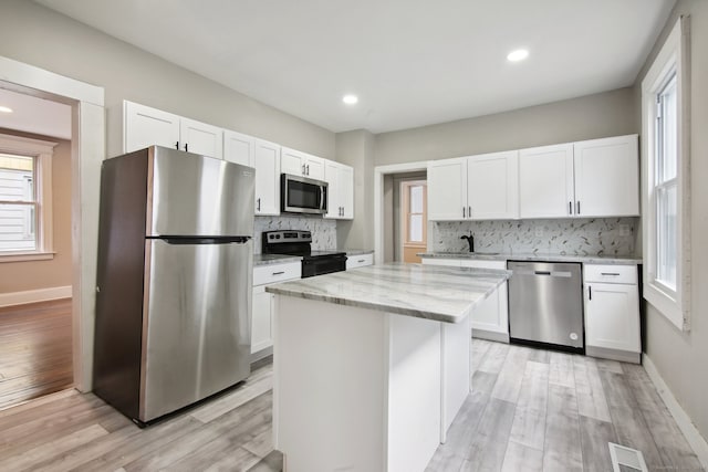 kitchen with appliances with stainless steel finishes, light hardwood / wood-style floors, backsplash, white cabinets, and a kitchen island