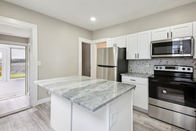 kitchen with light wood-type flooring, appliances with stainless steel finishes, white cabinetry, decorative backsplash, and a kitchen island