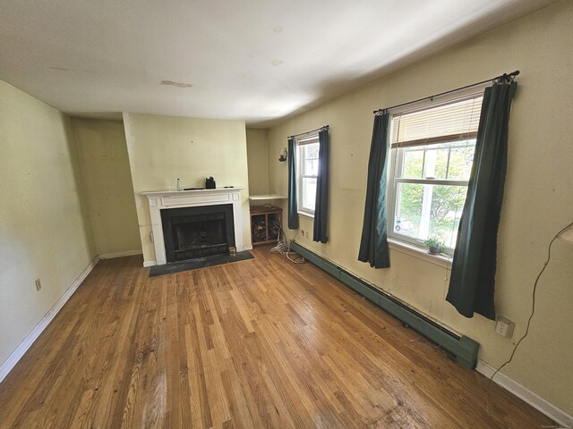 unfurnished living room with a baseboard heating unit and hardwood / wood-style floors