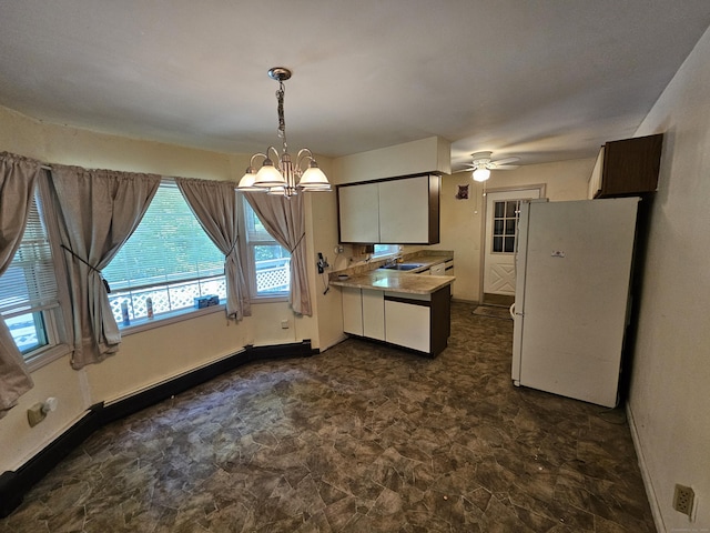 kitchen featuring white refrigerator, ceiling fan with notable chandelier, hanging light fixtures, and sink