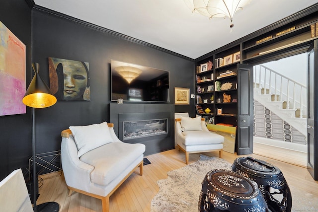 living area featuring crown molding, wood finished floors, and a glass covered fireplace