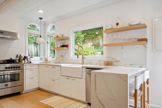 kitchen with stainless steel stove, open shelves, tasteful backsplash, a sink, and light stone countertops