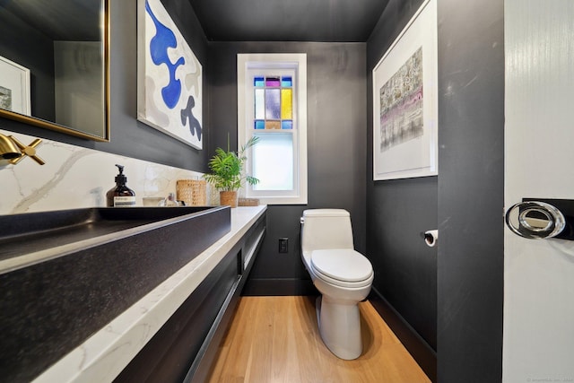 half bathroom with wood finished floors, toilet, vanity, and baseboards