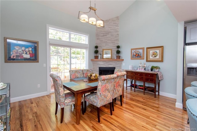 dining room featuring light wood-type flooring, an inviting chandelier, a large fireplace, and high vaulted ceiling