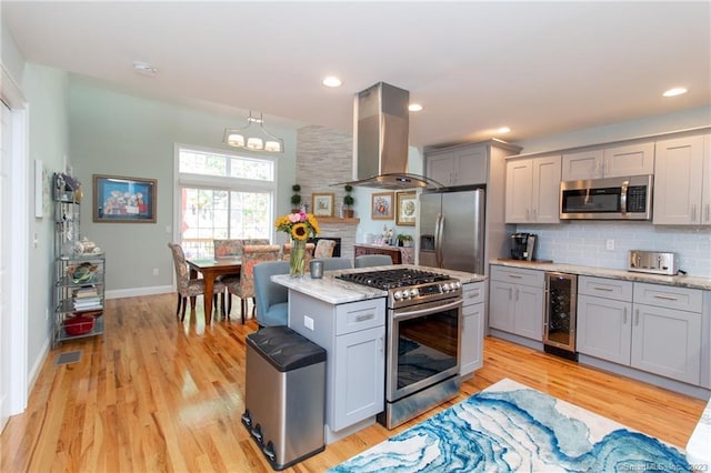 kitchen with gray cabinets, island range hood, backsplash, stainless steel appliances, and light hardwood / wood-style flooring