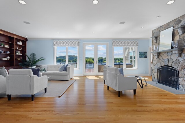 living room with a stone fireplace, light wood-type flooring, and french doors