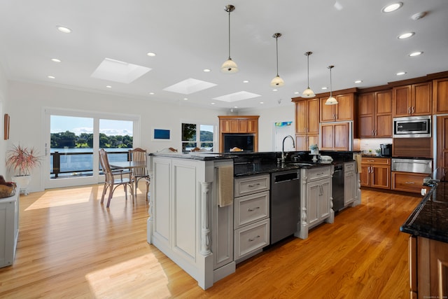 kitchen with appliances with stainless steel finishes, light wood-type flooring, dark stone counters, and a skylight