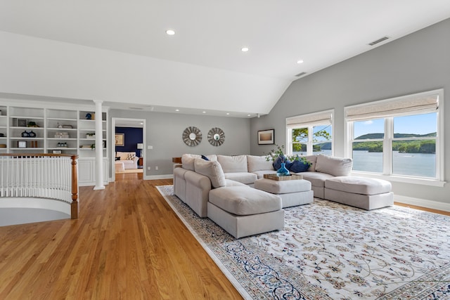 living room featuring decorative columns, a water view, light wood-type flooring, and vaulted ceiling