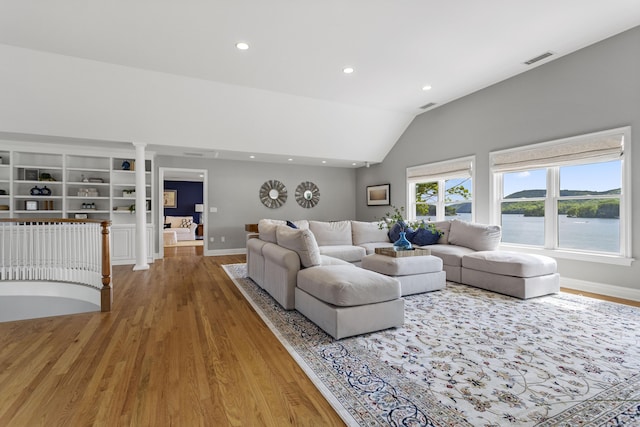 living room featuring a water view, wood-type flooring, high vaulted ceiling, and ornate columns