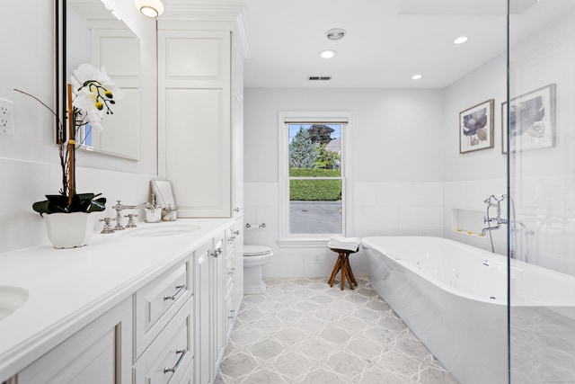 bathroom with tile patterned floors, a tub to relax in, toilet, tile walls, and vanity