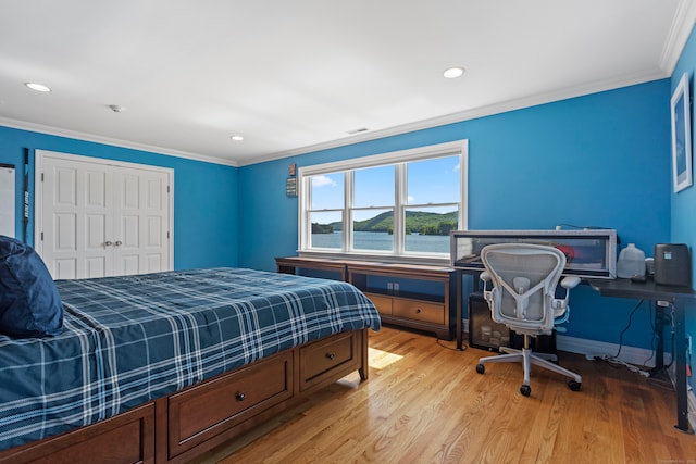 bedroom featuring crown molding, light hardwood / wood-style flooring, a water view, and a closet