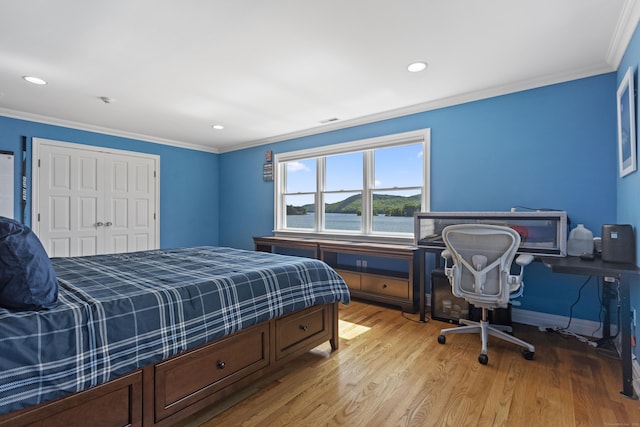 bedroom featuring crown molding, a water view, a closet, and light wood-type flooring