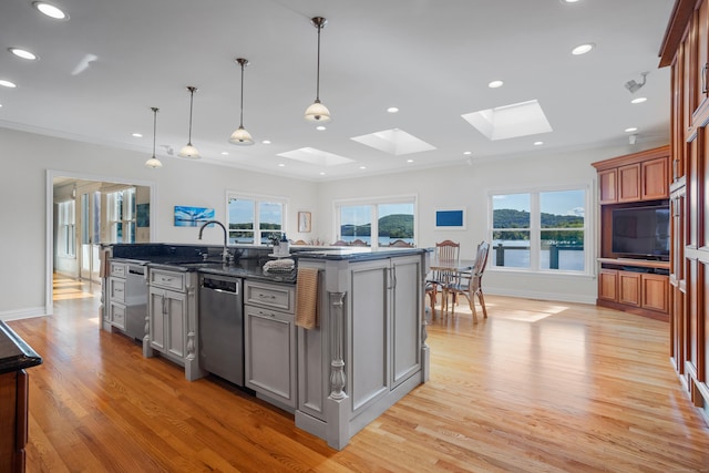 kitchen with dark stone counters, light hardwood / wood-style flooring, a kitchen island with sink, a skylight, and dishwasher