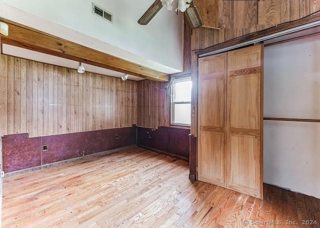 unfurnished room with ceiling fan, wood walls, beamed ceiling, and light wood-type flooring