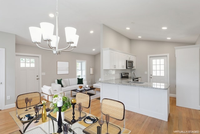 dining area with an inviting chandelier, sink, light hardwood / wood-style flooring, and vaulted ceiling