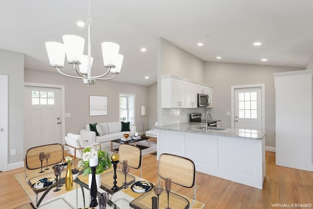 kitchen featuring pendant lighting, lofted ceiling, white cabinets, stainless steel appliances, and light stone countertops