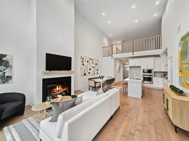 living area featuring a glass covered fireplace, light wood-style flooring, recessed lighting, and baseboards