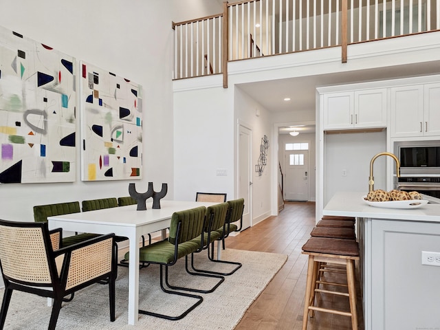 dining room featuring baseboards, light wood-style floors, and a towering ceiling