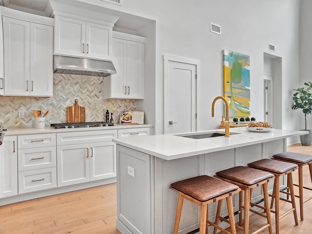 kitchen with visible vents, a kitchen bar, under cabinet range hood, a sink, and white cabinets