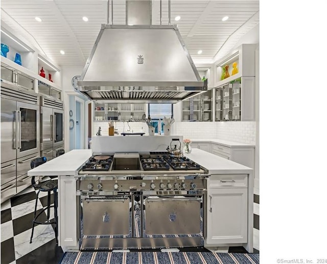 kitchen featuring a kitchen bar, tasteful backsplash, dark tile patterned floors, high quality appliances, and island exhaust hood