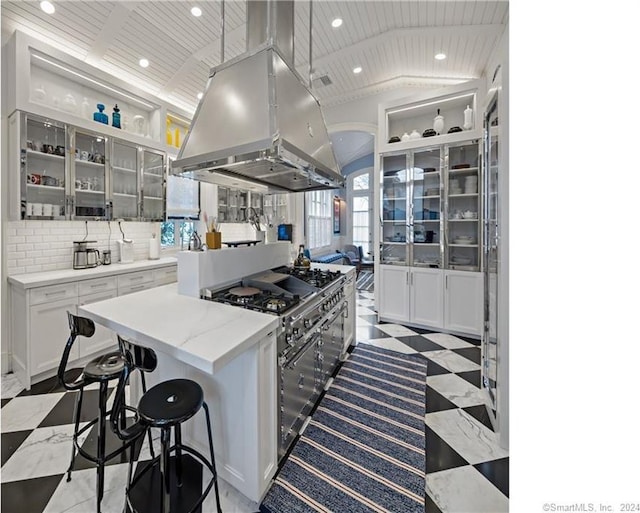 kitchen featuring lofted ceiling, light tile patterned floors, white cabinets, backsplash, and island exhaust hood