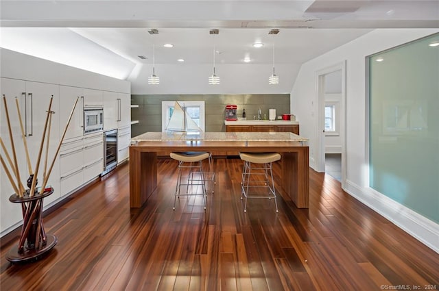 kitchen with lofted ceiling, dark wood-type flooring, built in microwave, hanging light fixtures, and a center island with sink