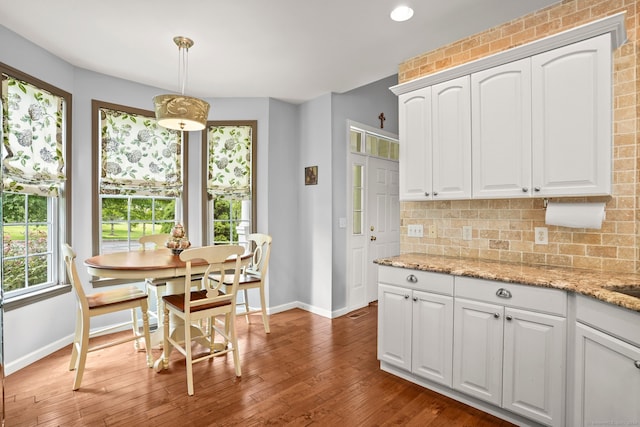 kitchen with pendant lighting, light stone counters, wood-type flooring, and white cabinets