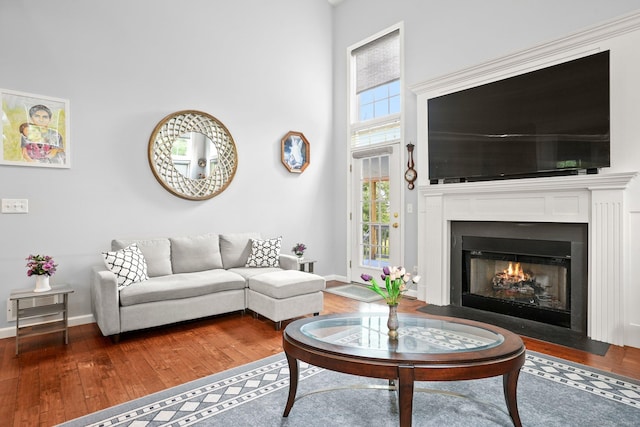 living room featuring a fireplace with flush hearth, wood-type flooring, a towering ceiling, and baseboards