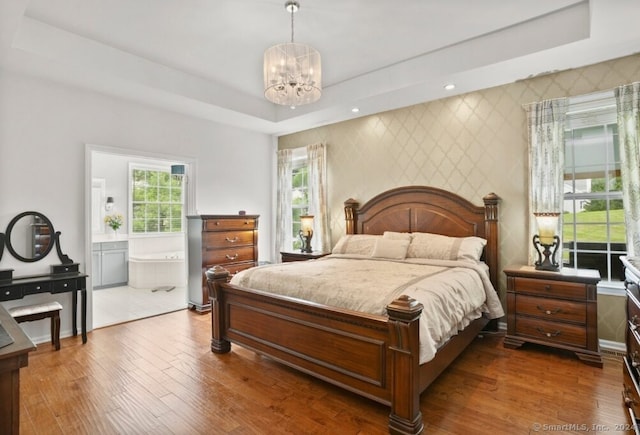 bedroom with a raised ceiling, an inviting chandelier, an accent wall, wood finished floors, and wallpapered walls