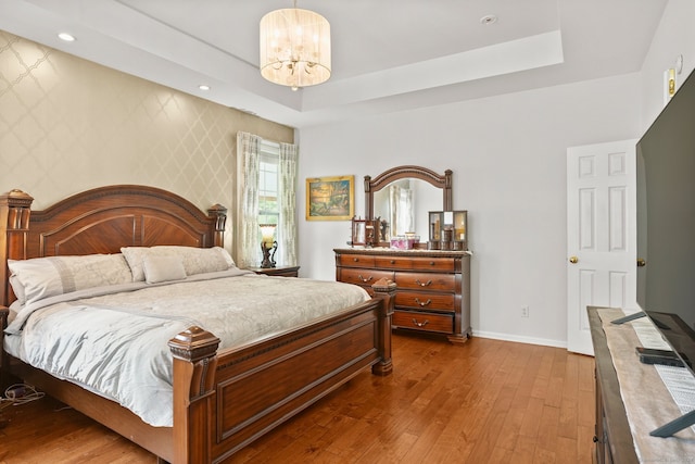 bedroom with an inviting chandelier, hardwood / wood-style flooring, and a raised ceiling