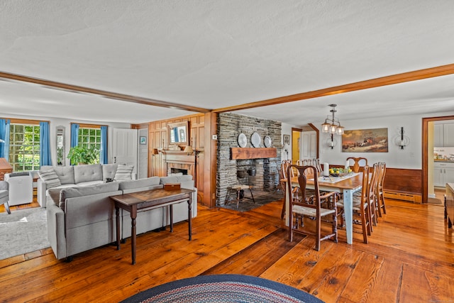 living room with hardwood / wood-style floors, a large fireplace, an inviting chandelier, a baseboard heating unit, and a textured ceiling