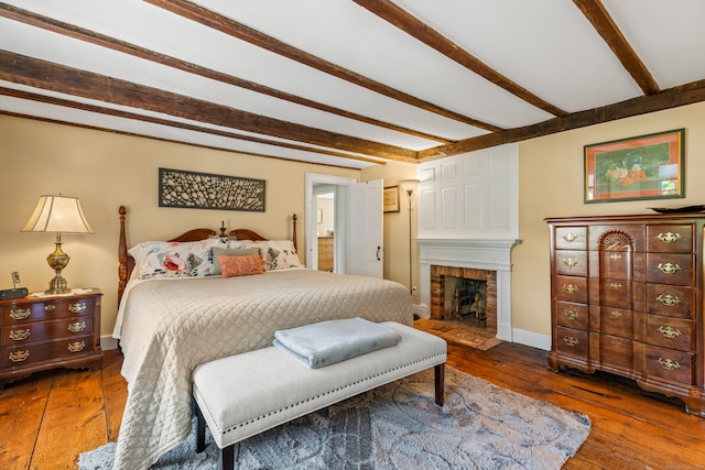 bedroom with beamed ceiling, hardwood / wood-style flooring, and a brick fireplace