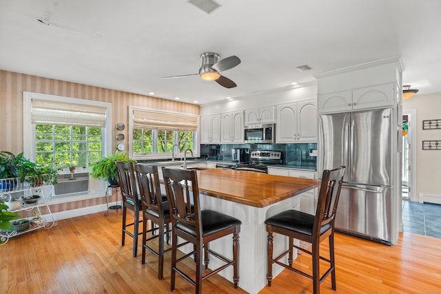 kitchen featuring stainless steel appliances, light hardwood / wood-style floors, white cabinets, ceiling fan, and a breakfast bar