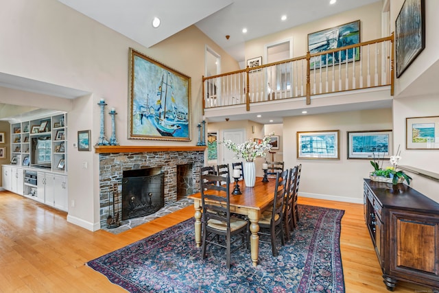 dining room featuring a high ceiling, a stone fireplace, and light hardwood / wood-style flooring