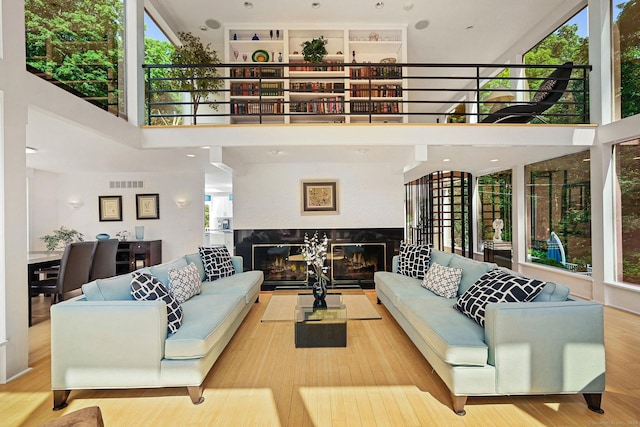 living area featuring wood finished floors, a high ceiling, a multi sided fireplace, and visible vents