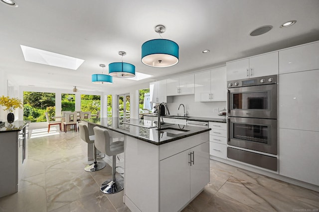 kitchen featuring a breakfast bar, marble finish floor, a skylight, stainless steel double oven, and white cabinetry