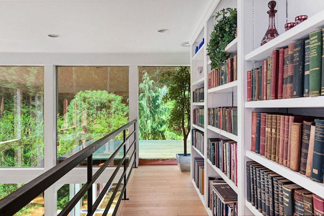 interior space with wall of books, wood finished floors, and recessed lighting