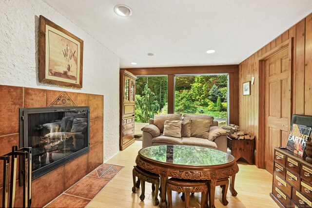 dining space with a tiled fireplace, wood walls, a textured ceiling, and light hardwood / wood-style flooring