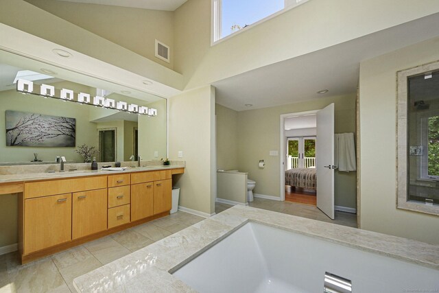 bathroom featuring a towering ceiling, vanity, toilet, and plenty of natural light