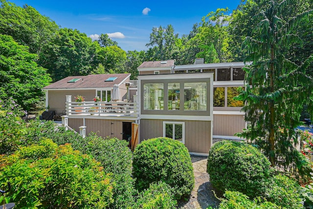 rear view of house with a chimney, a wooden deck, and a sunroom