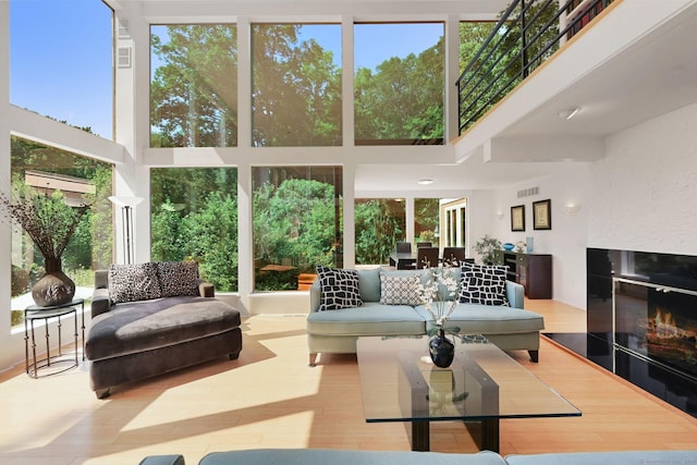 interior space featuring a glass covered fireplace, visible vents, a towering ceiling, and wood finished floors