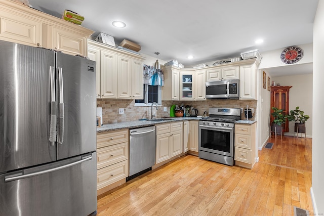 kitchen with appliances with stainless steel finishes, pendant lighting, sink, light hardwood / wood-style floors, and light stone countertops