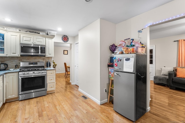 kitchen featuring light stone counters, backsplash, stainless steel appliances, and light hardwood / wood-style floors