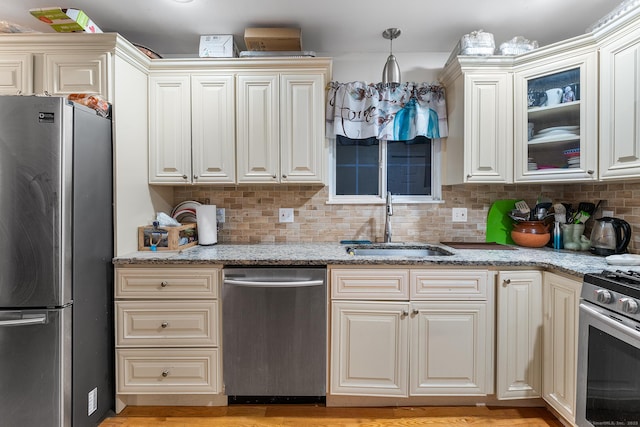 kitchen with light stone counters, appliances with stainless steel finishes, sink, and pendant lighting