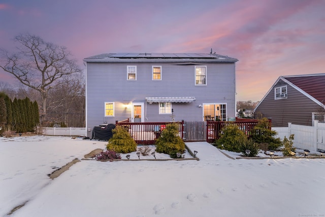 snow covered house with a wooden deck and solar panels