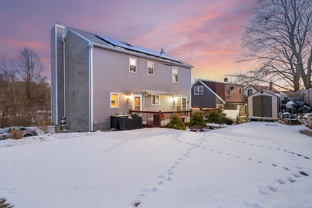 snow covered rear of property featuring a storage shed, a deck, and solar panels