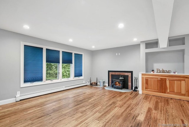 unfurnished living room with a wood stove, light hardwood / wood-style flooring, and a baseboard heating unit